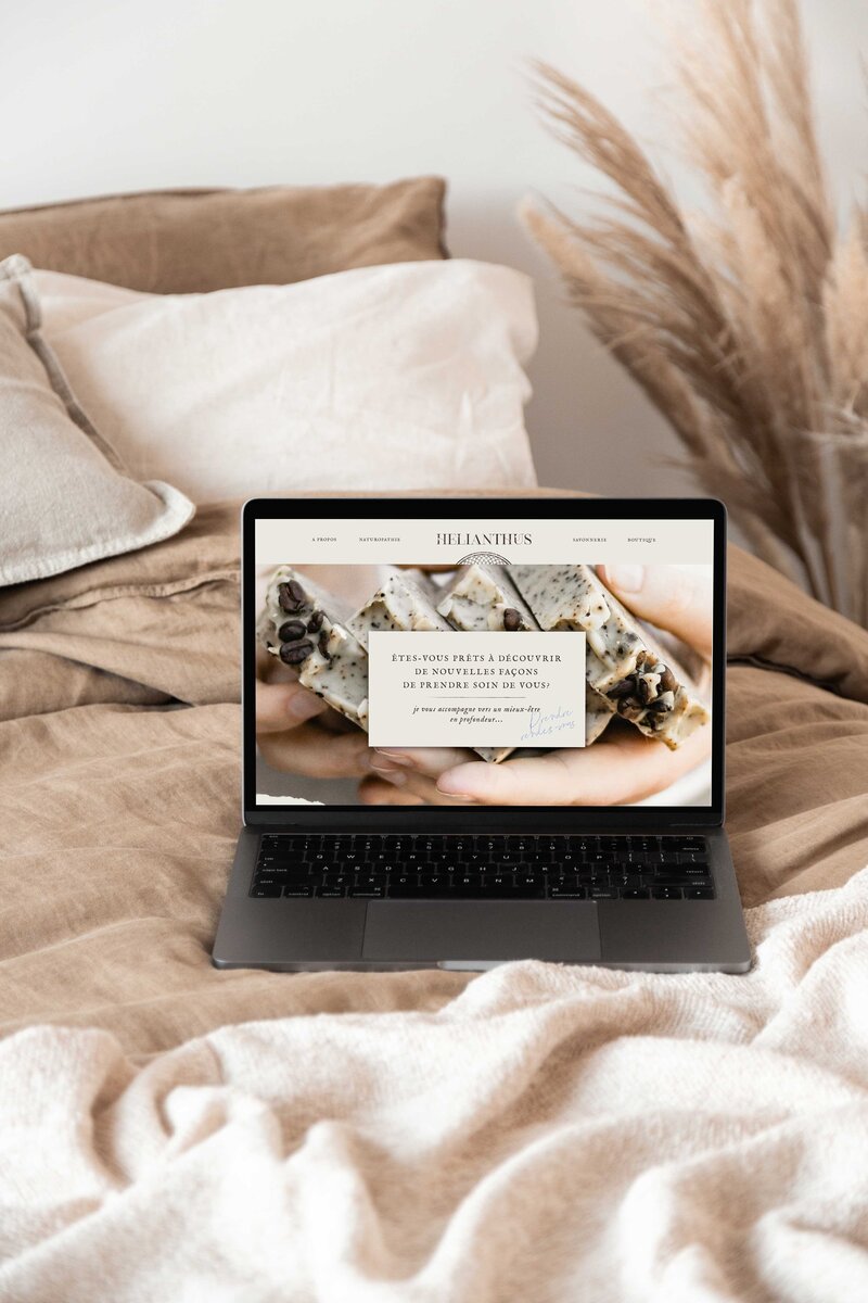 laptop on a bed with linen sheets displaying a naturopath website and soap maker