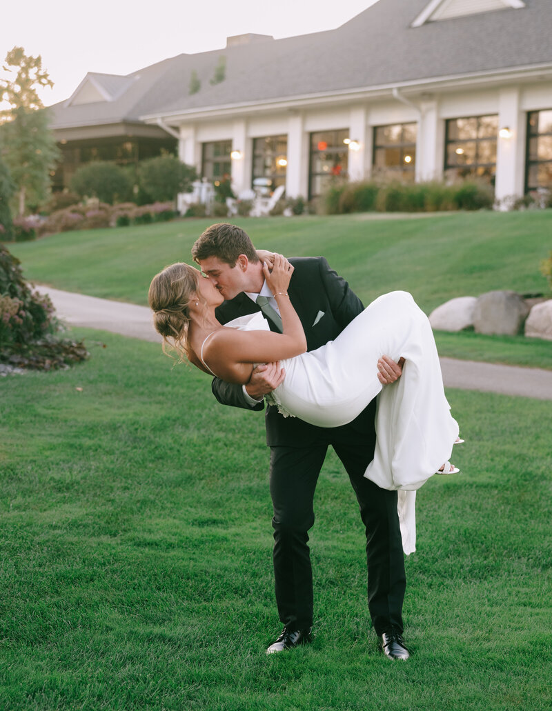 A groom in a black suit picks up his bride and kisses her at golden hour at The Union at Railside on their wedding day.