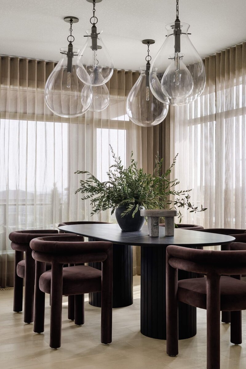 Oval black dining room table with chocolate velvet chairs and clustered glass pendants. 