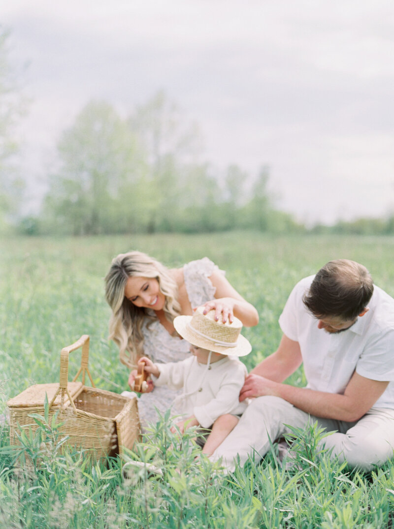 Mother, Father and toddler sitting together in a field with picnic basket.