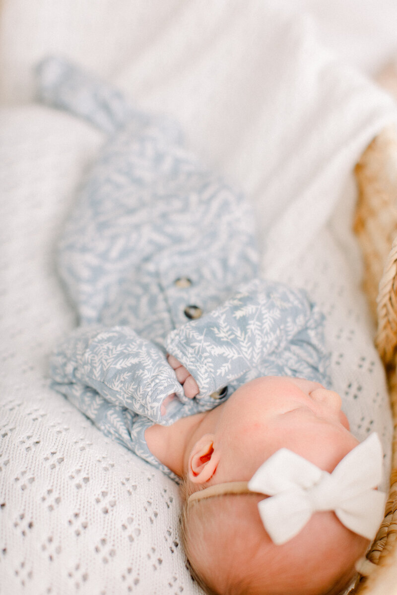 Newborn baby in blue and white floral Lou Lou & Co knotted onesie sleeps soundly on a crochet blanket in a moses basket by NH newborn photographer Fieldstone Studio