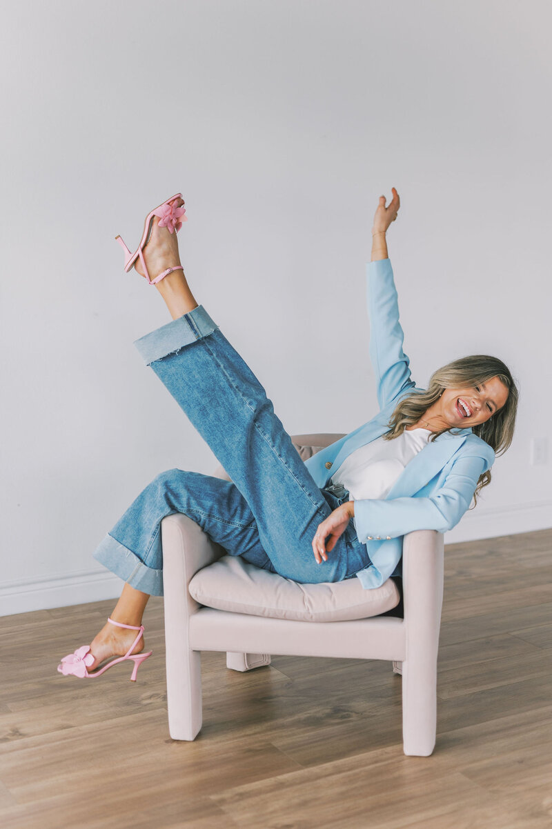 Headshot of Lindsey Kristian in a blue blazer and jeans sitting sideways in a chair with one arm and leg raised