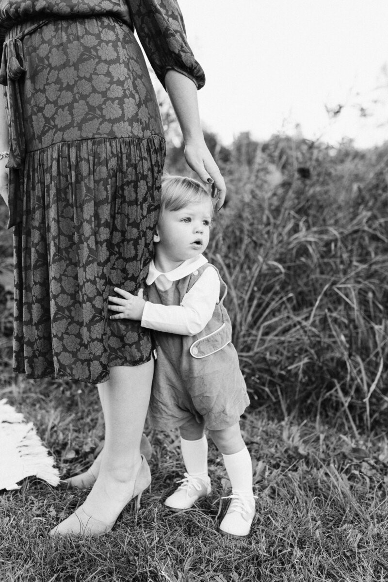 sweet little boy holds onto his mom's leg while she lovingly pats him on the head