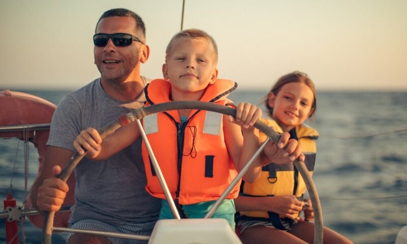 Mann mit Sonnenbrille am Ruder mit seinem Sohn und Tochter sitzt daneben
