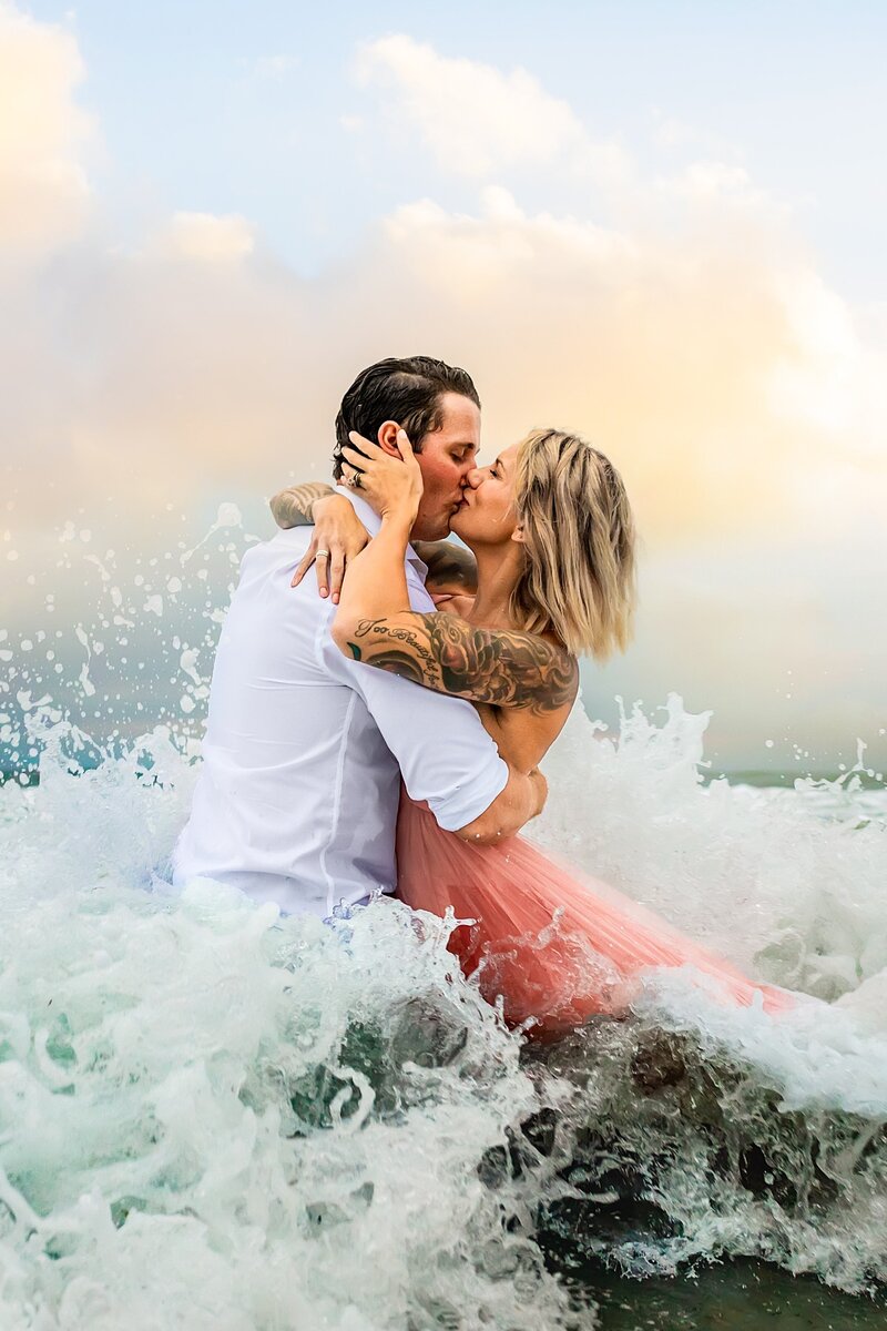 Enagement Portrait of a couple kissing with waves splashing around them in Carlsbad California