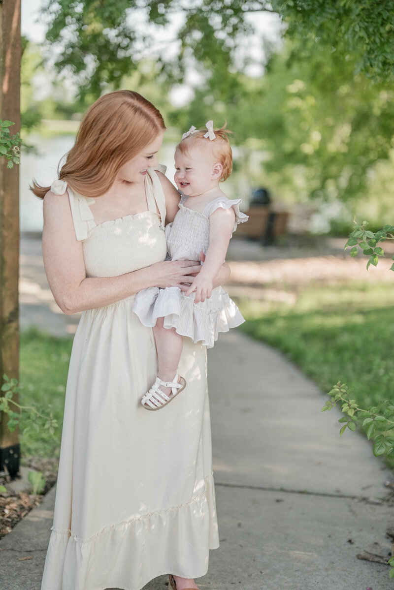 Red-haired mother smiling at her daughter while holding her during a warm-weather family session captured by a Kansas City family photographer.
