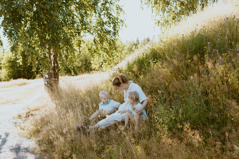 Äiti ja hänen kaksi poikaansa istuvat maassa puun varjossa kesällä Käpylässä Helsingissä