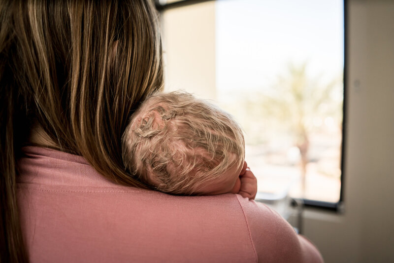 Baby with blonde hair sleeping on the shoulder of a woman