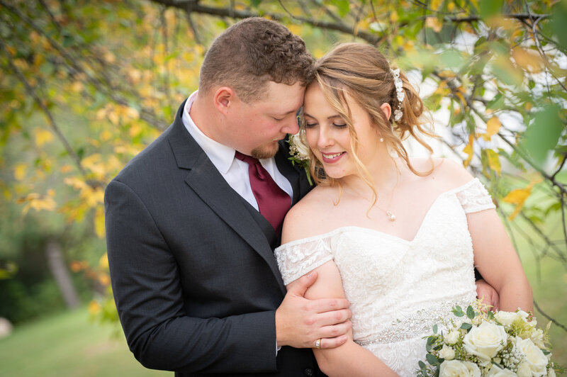 bride and groom with their foreheads together in front of yellow tree