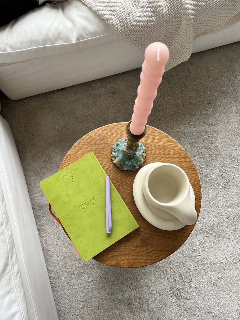 Overhead shot of a lime green notebook witha a light purple pen. A cream  colored mug is on the table beside.