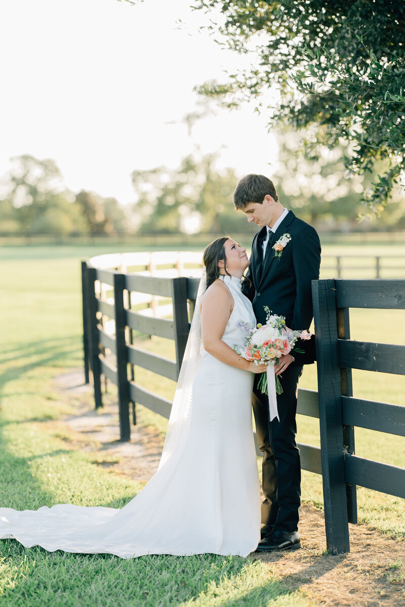 bride and groom embracing beside the fence of a horse pasture