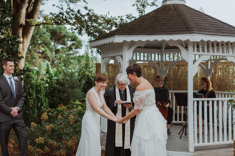 LGBTQ couple laughing and holding hands during their wedding ceremony.
