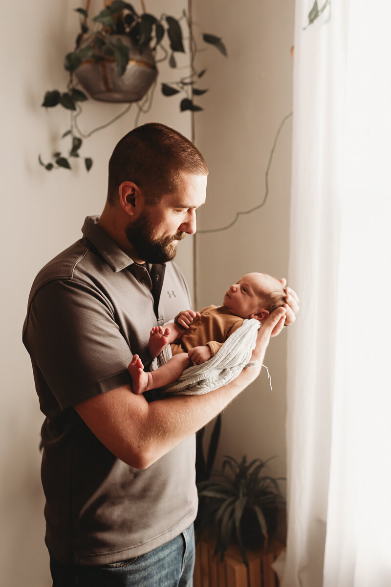 a dad has all the feels during a newborn studio session as he gazes lovingly at his son. 