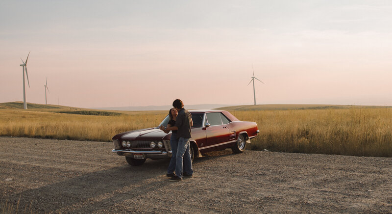 A couple dances in front of a vintage car outside.