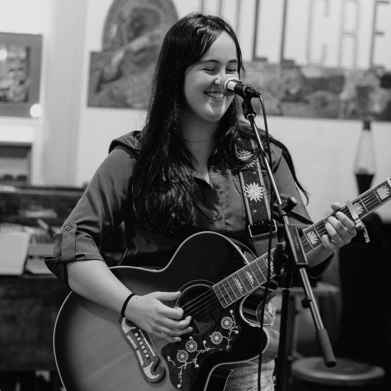 Woman smiles and plays guitar at Hillcrest Coffee