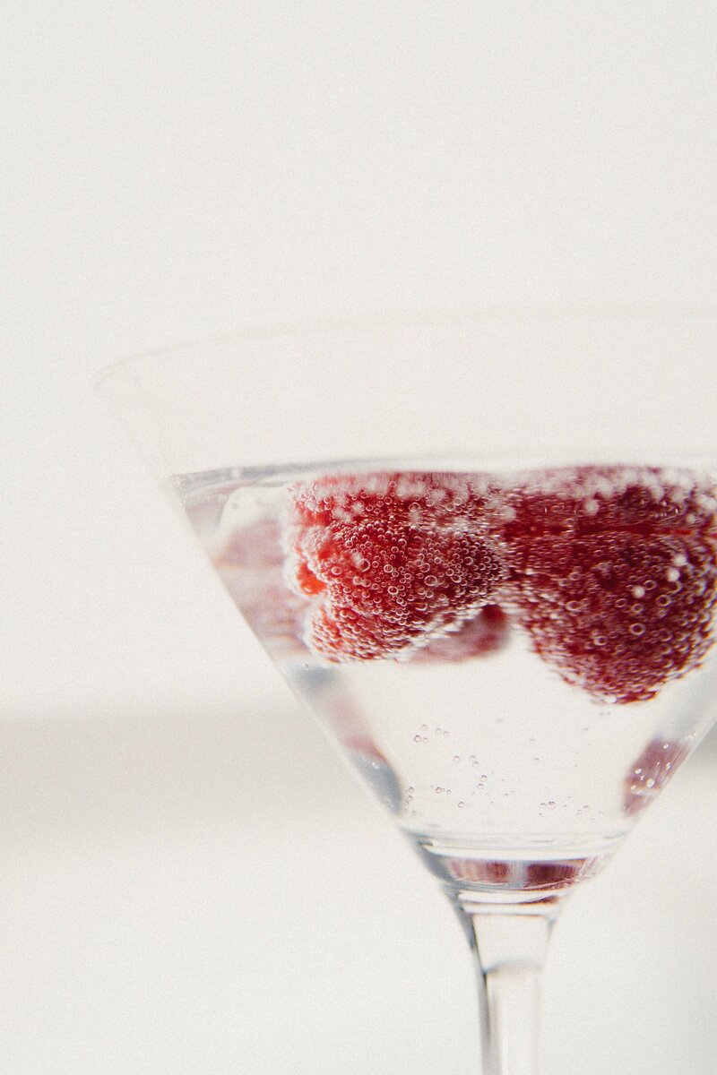 a martini glass filled with a fizzy clear liquid that has raspberries floating in it and covered in bubbles for contact page socialfizz