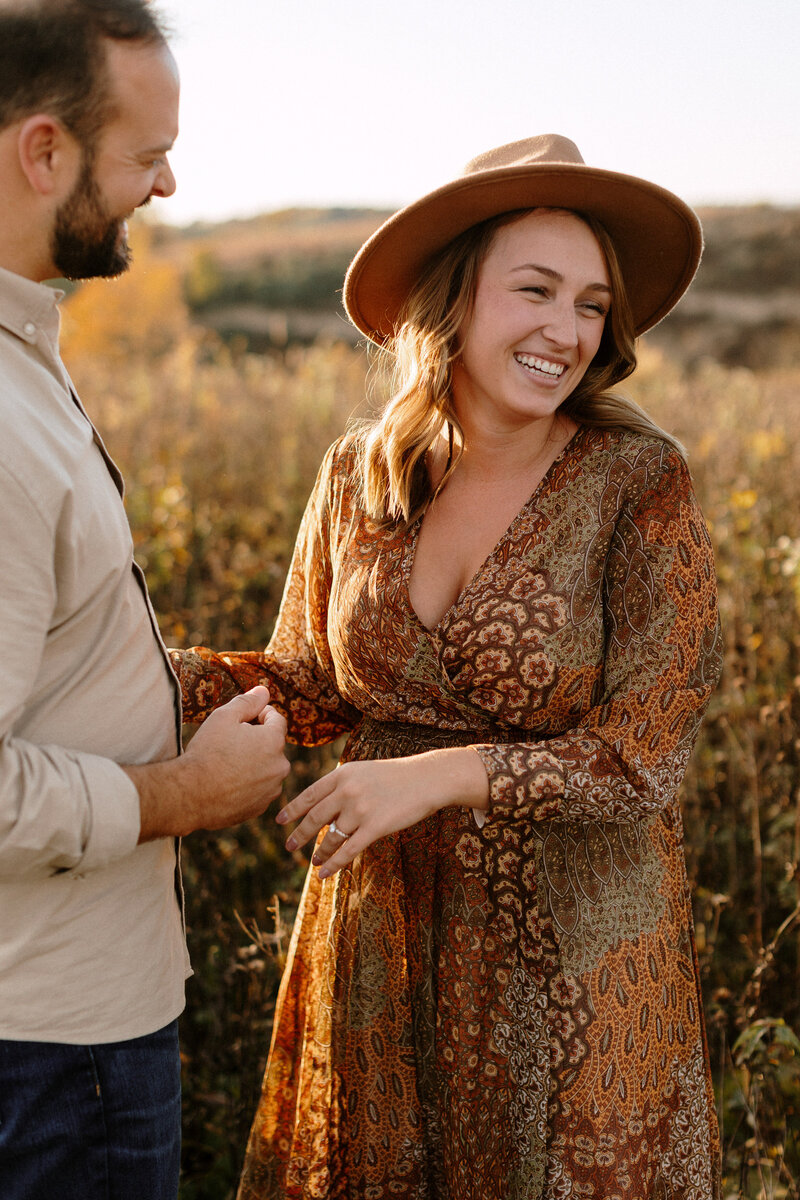 A couple shares a loving moment in a scenic fall field, surrounded by warm autumn colors during their engagement photo shoot.