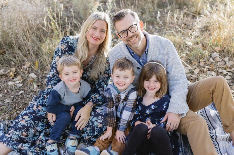 A family of five sits in the grass, cozy and smiling at the camera.
