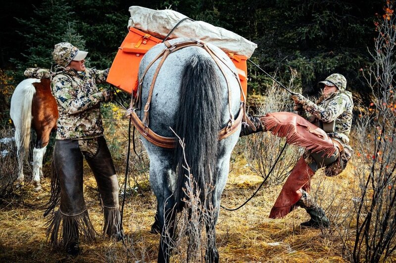 Two girls are standing beside a big horse tugging at the ropes as they pack