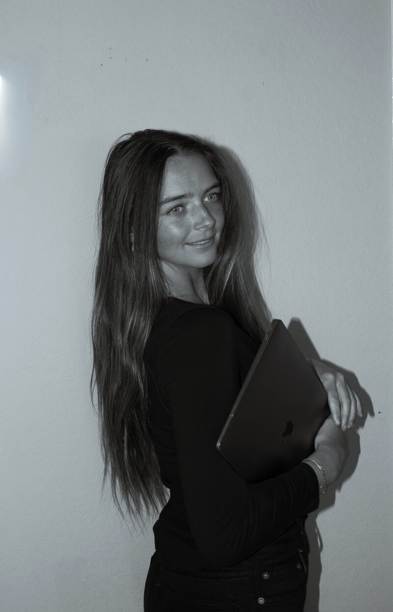 Black and white photo of Ava, the owner of The Charmed Post, holding a laptop looking off in to the distance