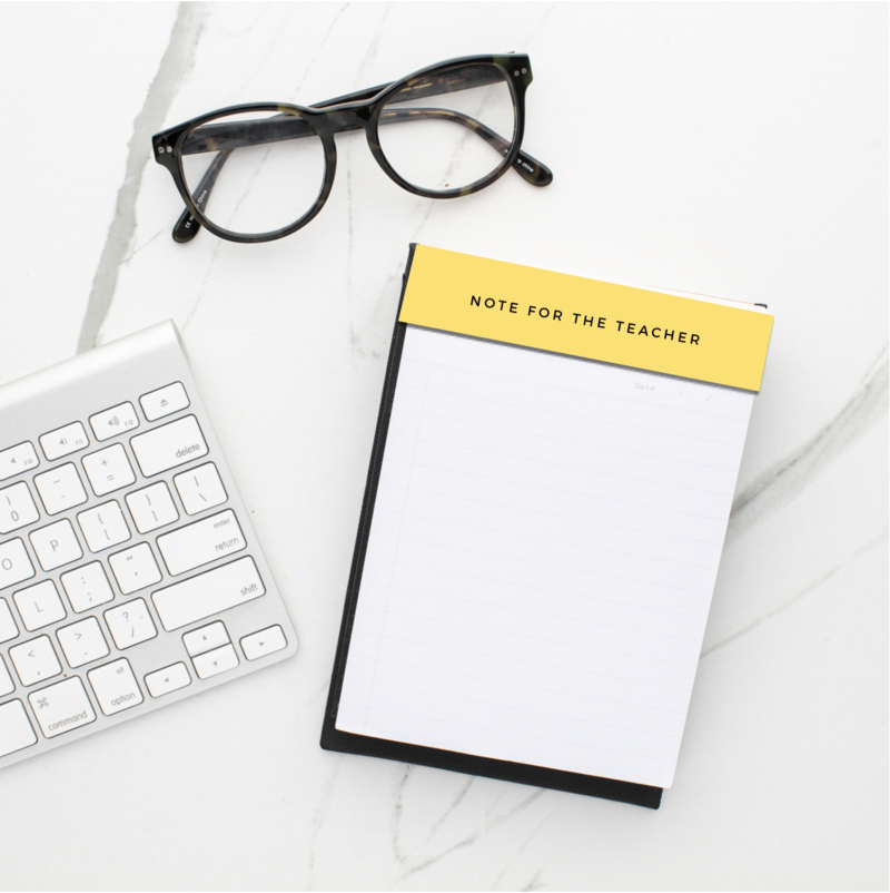 A teacher notepad sits beside a keyboard and a pair of glasses on a marble desk.