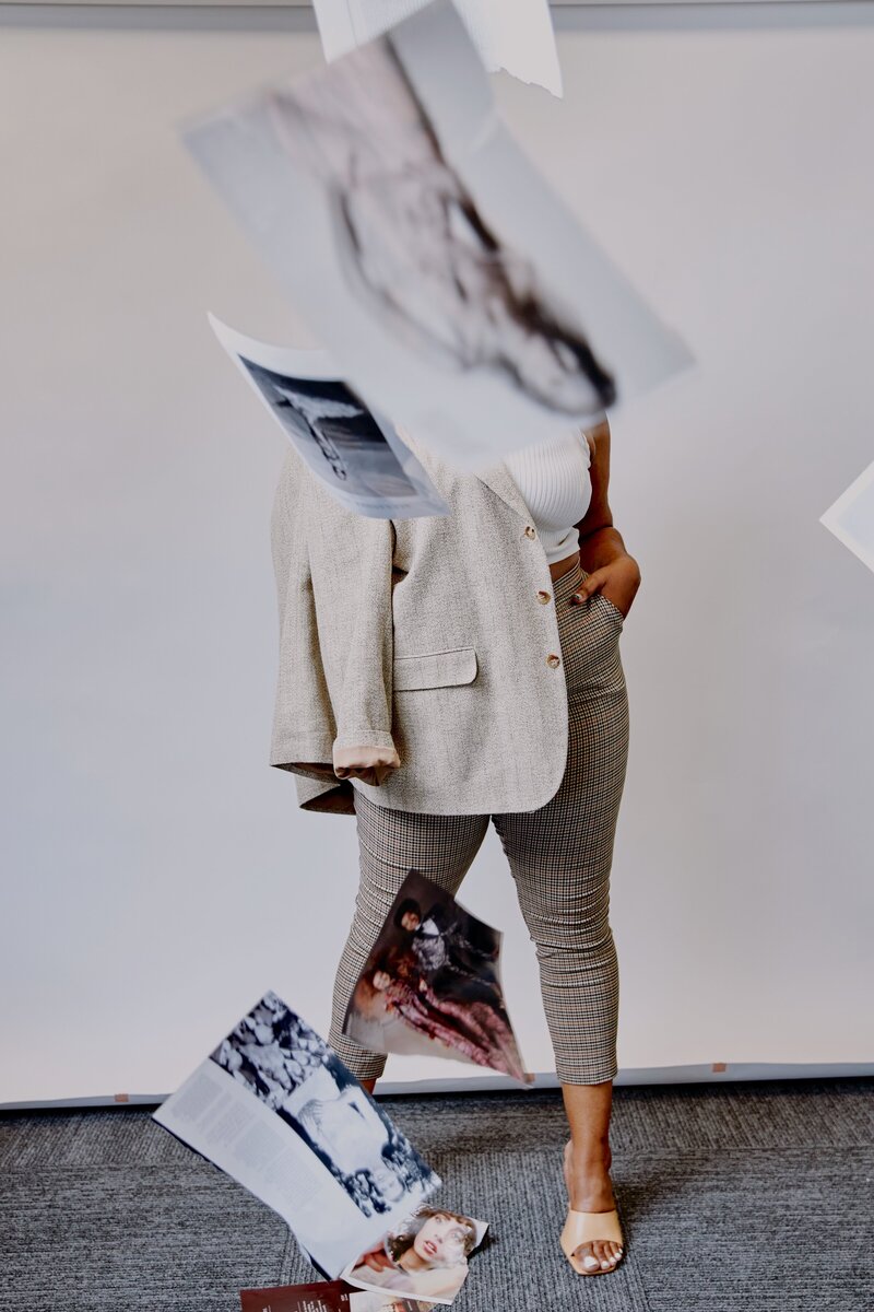 Artistic model with flying magazine pages wearing neutral business casual fashion.