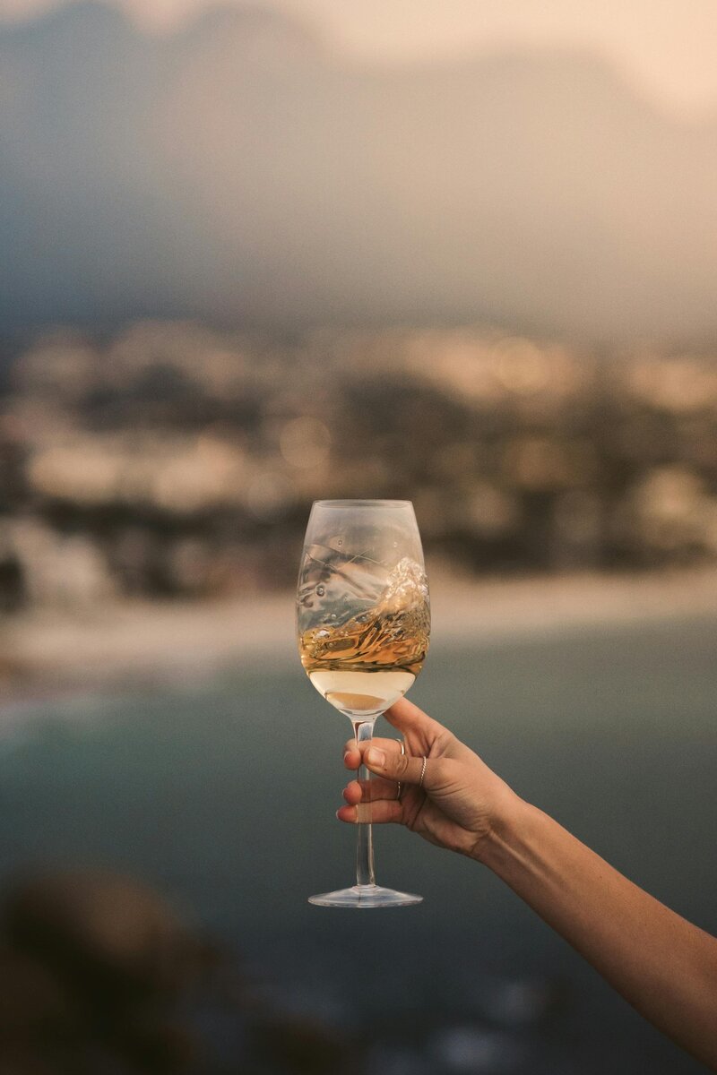 Vacation moment: enjoying white wine while overlooking a stunning coastal landscape. Tailored Oasis Travel Co.