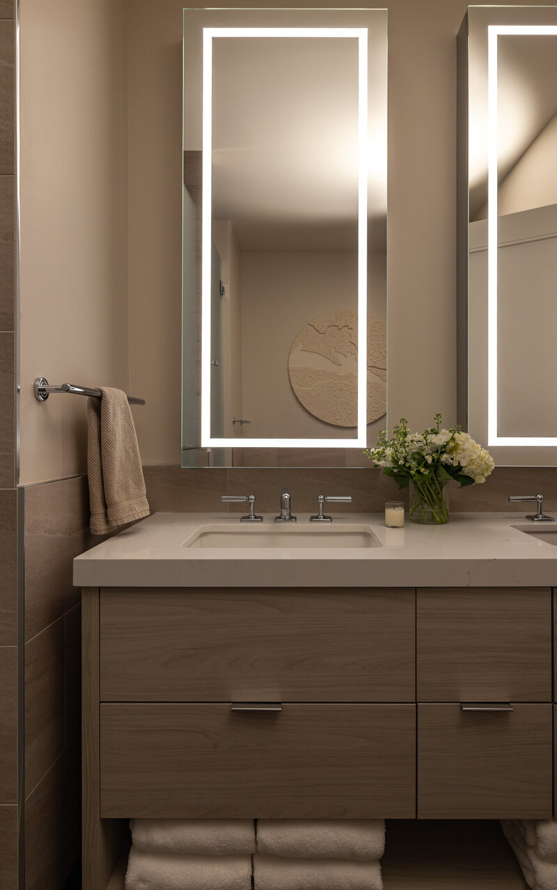 A close-up image of a modern primary bathroom with marble countertops, white oak cabinetry, and pre-lit mirrors in Park City, Utah. Designed by Sister Studio Interior Design.