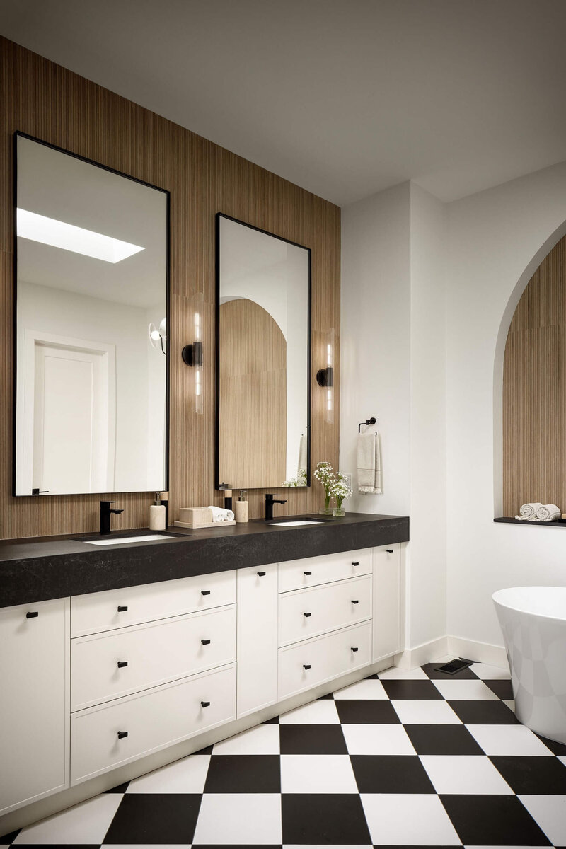 A gorgeous ensuite with black dekton counter tops, natural cream cabinets, black accents and a fluted backsplash tile paired with black and white checker tile. 