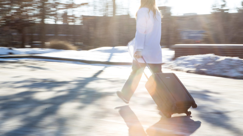 sonographer in scrubs and a lab coat walking outside pulling an equipment case