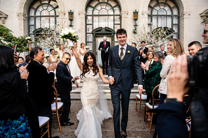 Historic Flood Mansion wedding photography featuring newlyweds' joyful recessional with ornate arched windows and celebrating guests