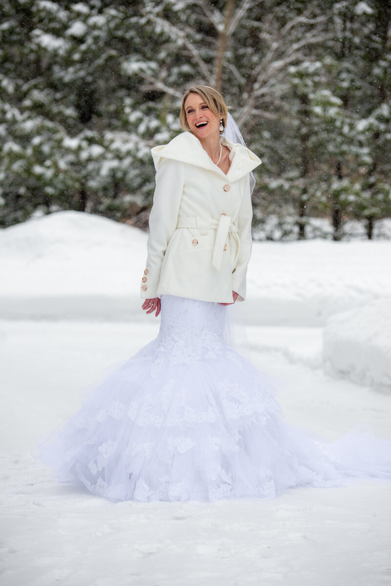 A bride posing in the snow in her dress and winter jacket in Kitchener, Ontario.
