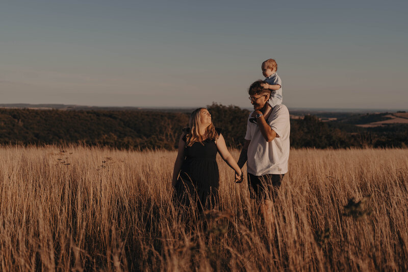 Parents, mother and father kissing and hugging there newborn on a summers day in Surrey