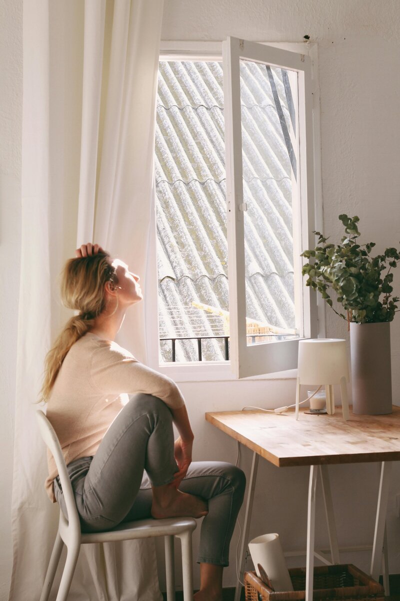 A woman sitting at a table facing the sun out her window