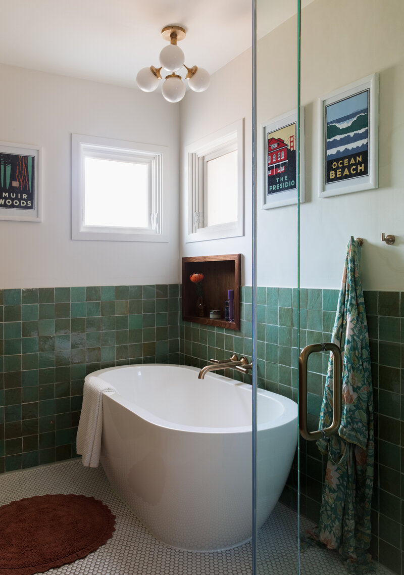 Bold green zellige tile and a freestanding tub with brass hardware. A wood trimmed bath niche above and nautical art on the walls