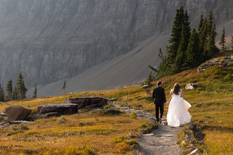 Bride and Groom walking hand in hand down a mountain path.