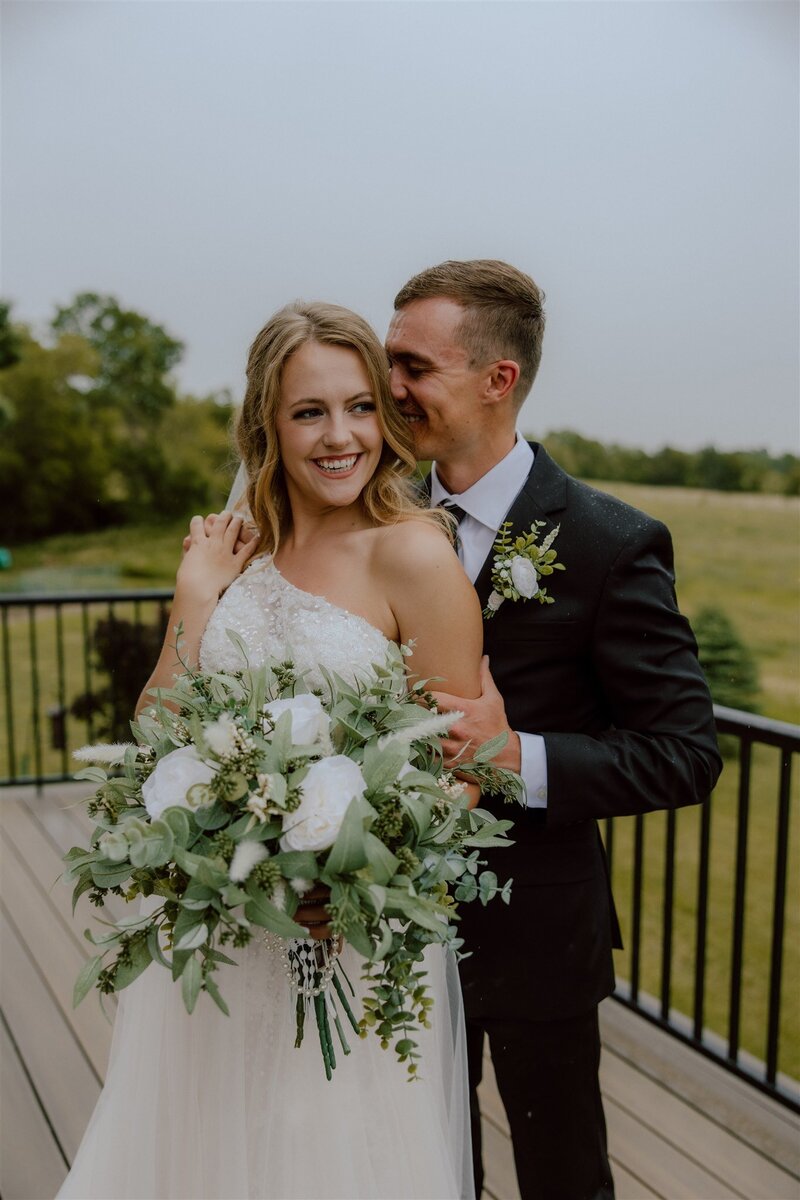 Bride and groom holding the bride's bouquet in an outdoor wedding setting, with soft natural light highlighting the couple's love and the delicate flowers in the bouquet.