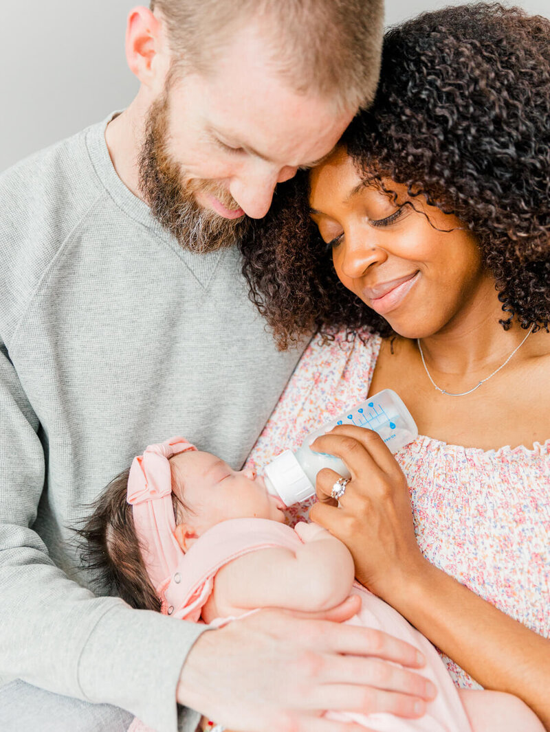 Mom sitting with dad while giving their baby a bottle