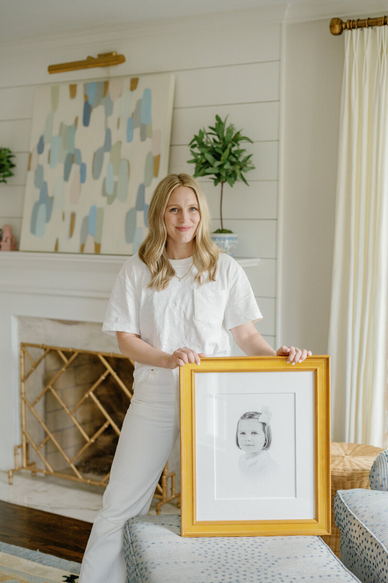 Lynnesy holding gold frame of heirloom print in a living room