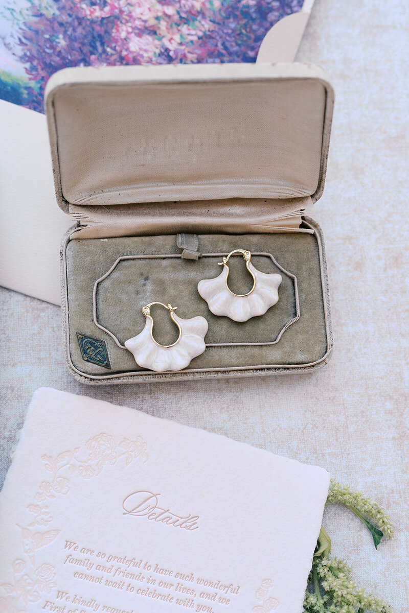 Grey Cove Designs romantic wedding flatlay featuring sculptural white floral earrings in a vintage velvet ring box, paired with blind embossed and letterpressed stationery and a soft painterly backdrop.