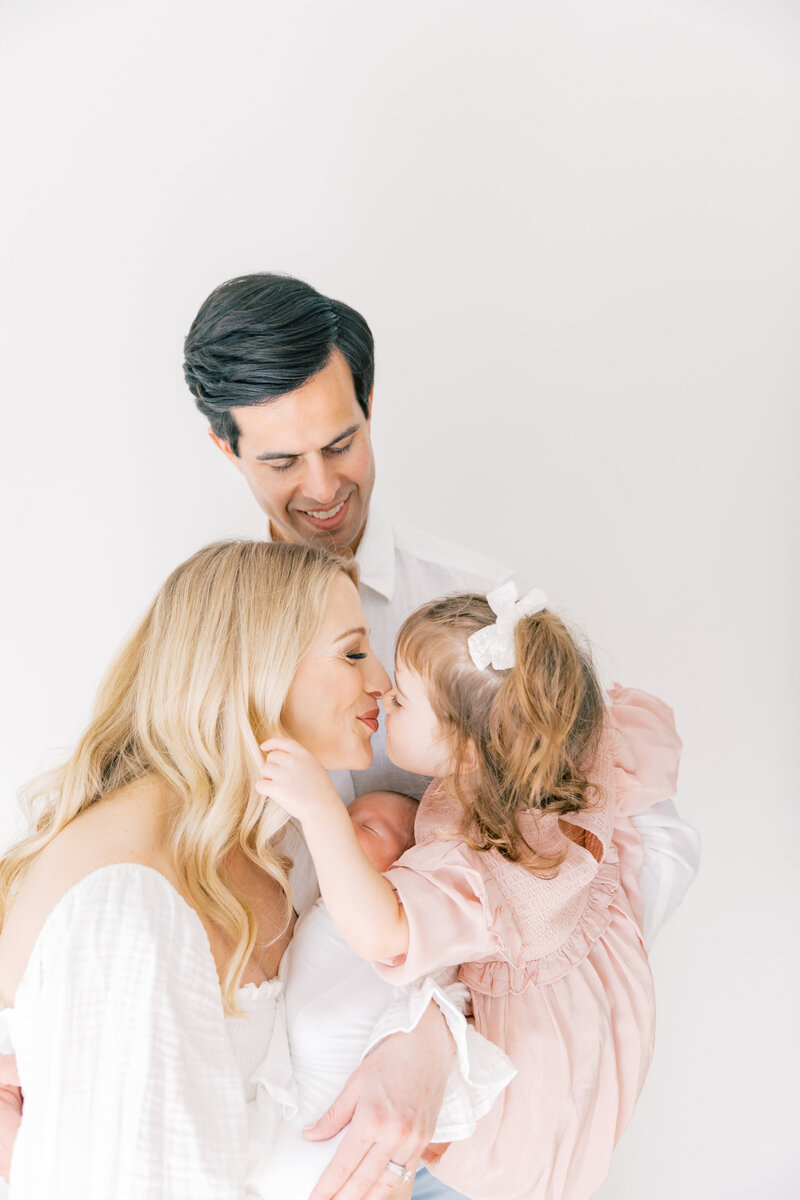 A mom kisses her toddler daughter while holding her newborn baby for a Charlotte Family Photographer