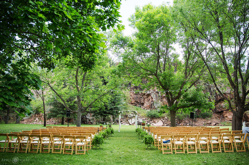 Wedding ceremony set up on the green lawn with beautiful trees and cliff backdrop at Riverbend in Lyons Colorado