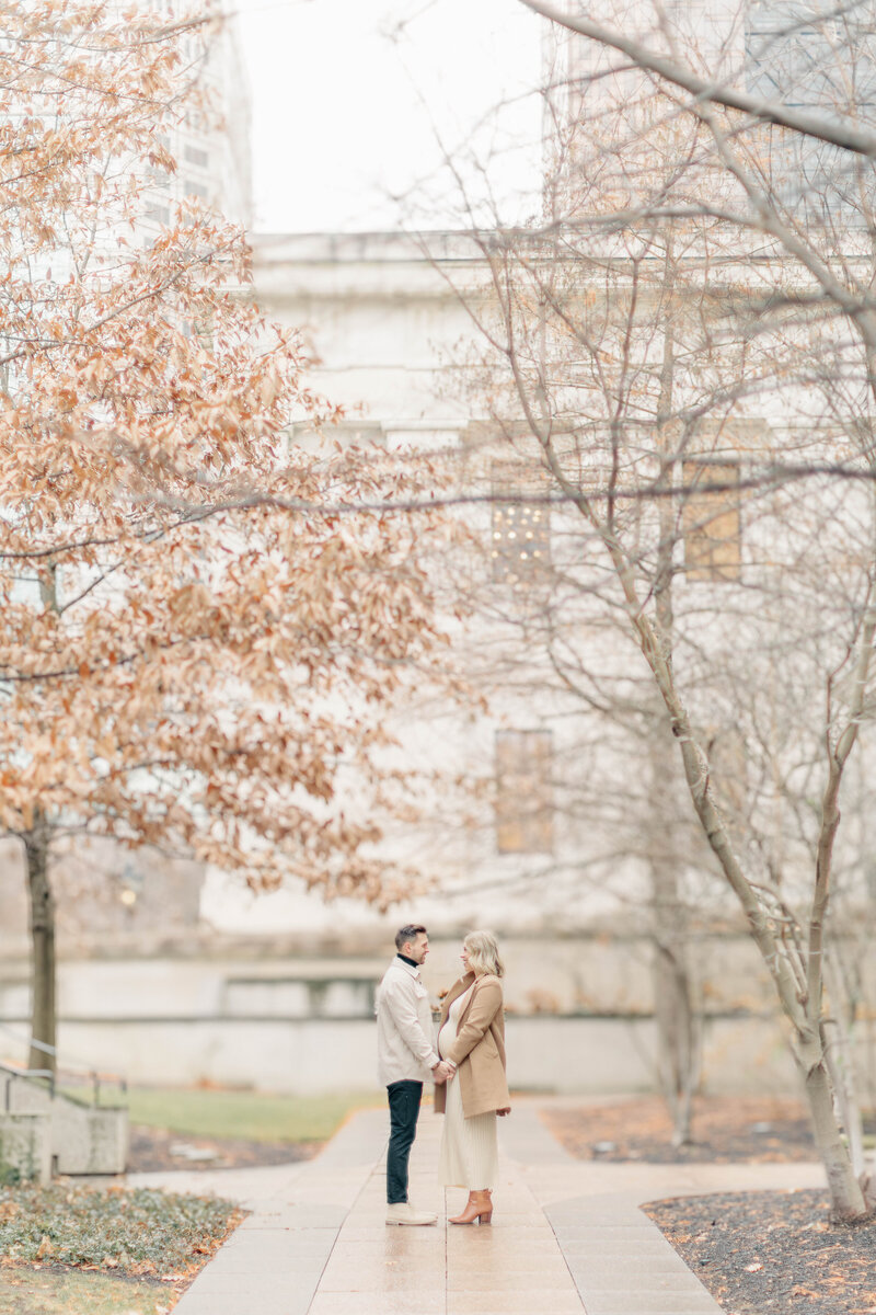 Expectant couple standing on a path lined with fall trees during their Kansas City maternity session.