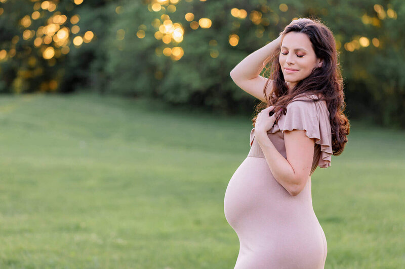 A mom-to-be posing for portraits in a tan dress at a park at sunset.