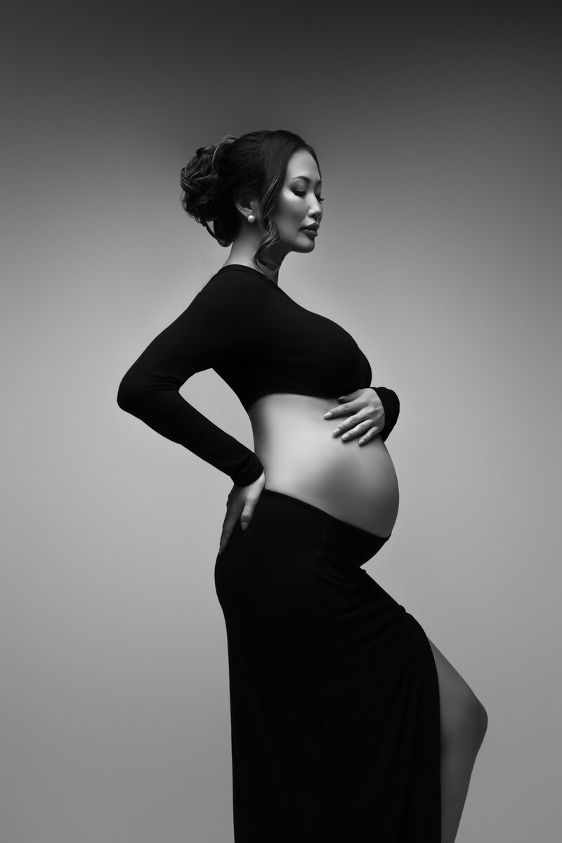 Pregnant woman black and white  black two piece dress with pregnant belly showing woman holding her belly with hair tied up