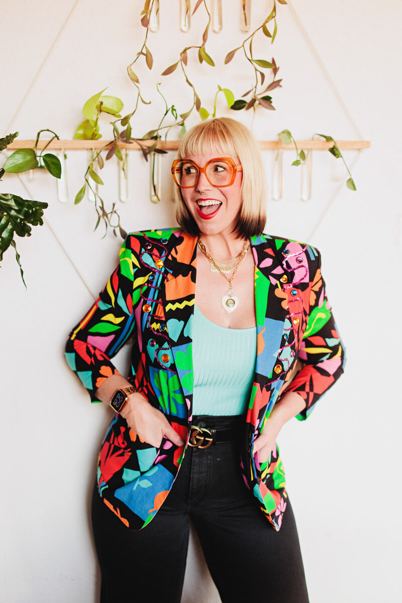 Heather a hair stylist in Eugene stands with her hands in her jacket pocket and smiles at the camera.