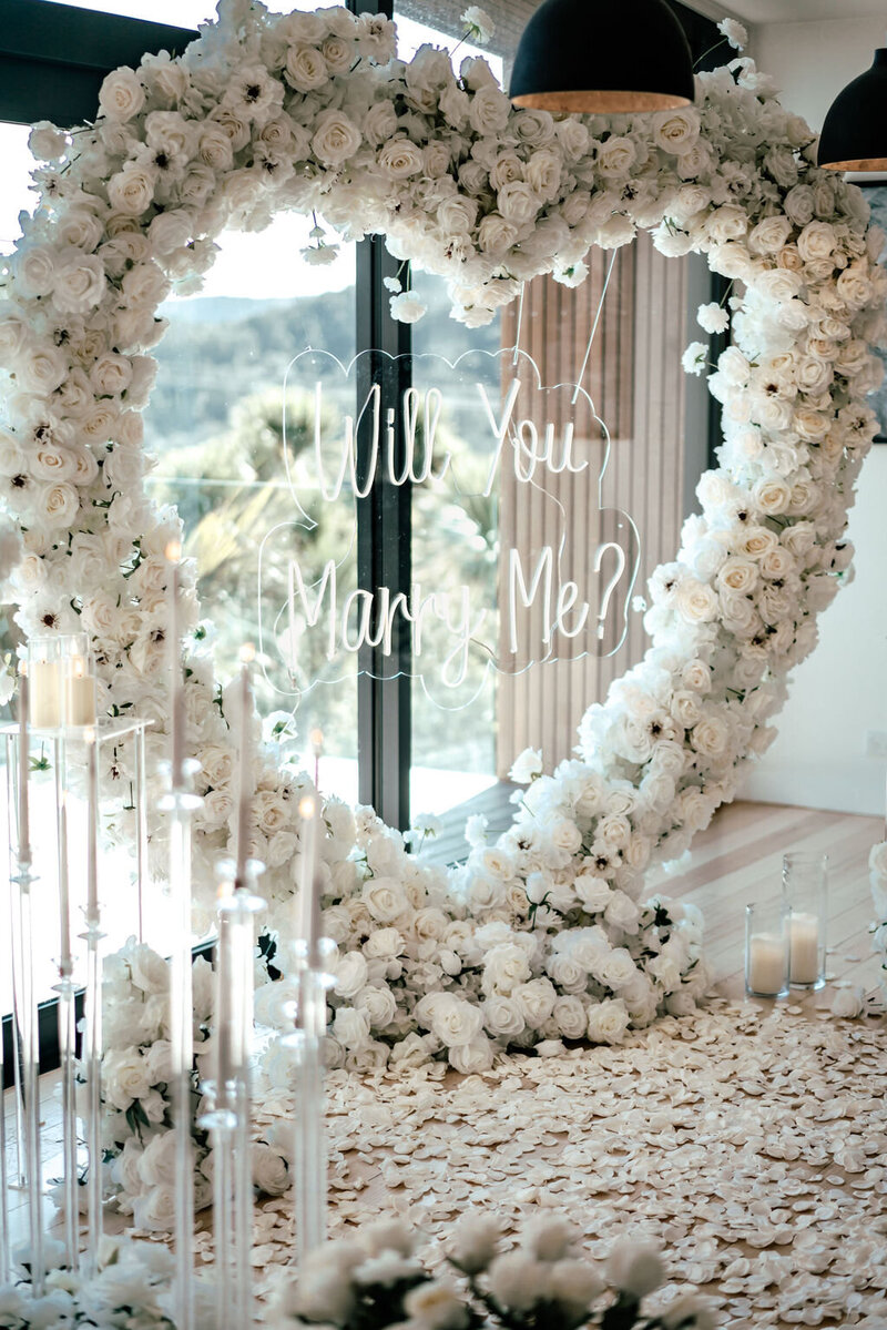 Groom-to-be proposing with a floral arch and rose petals in Auckland, photographed by Zanthe Vorsatz, proposal photographer.
