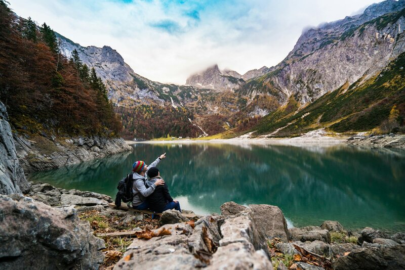Image of two people cuddling at a lake with one point up at the mountains