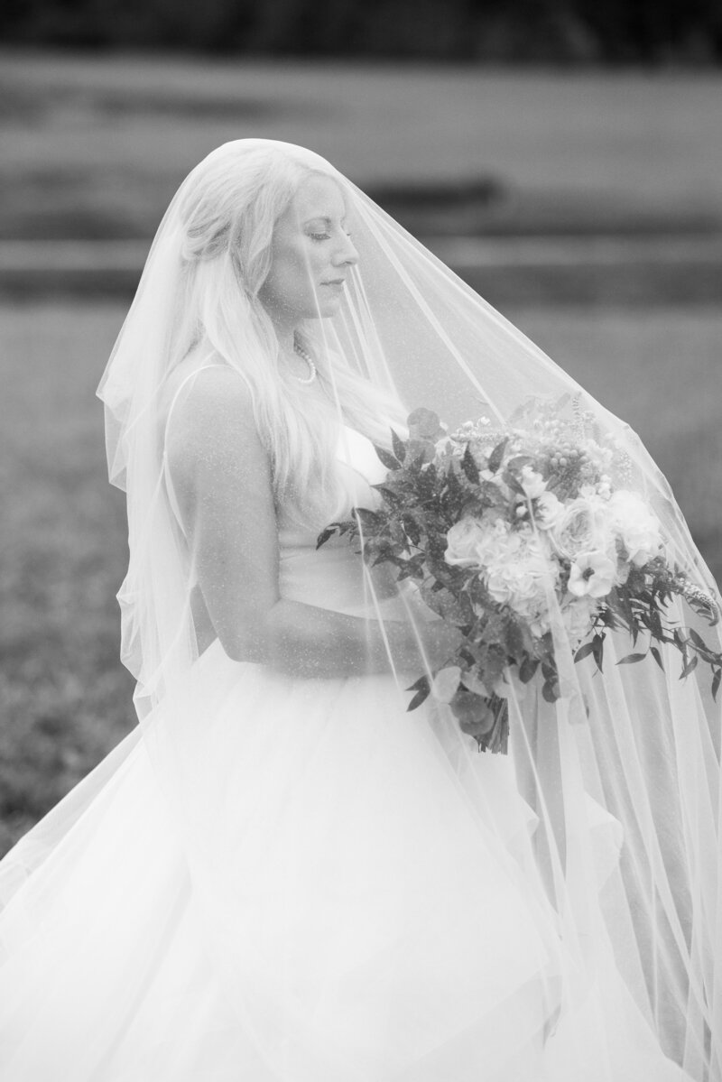 Black and white image of a bride with her veil over her face while holding her bouquet