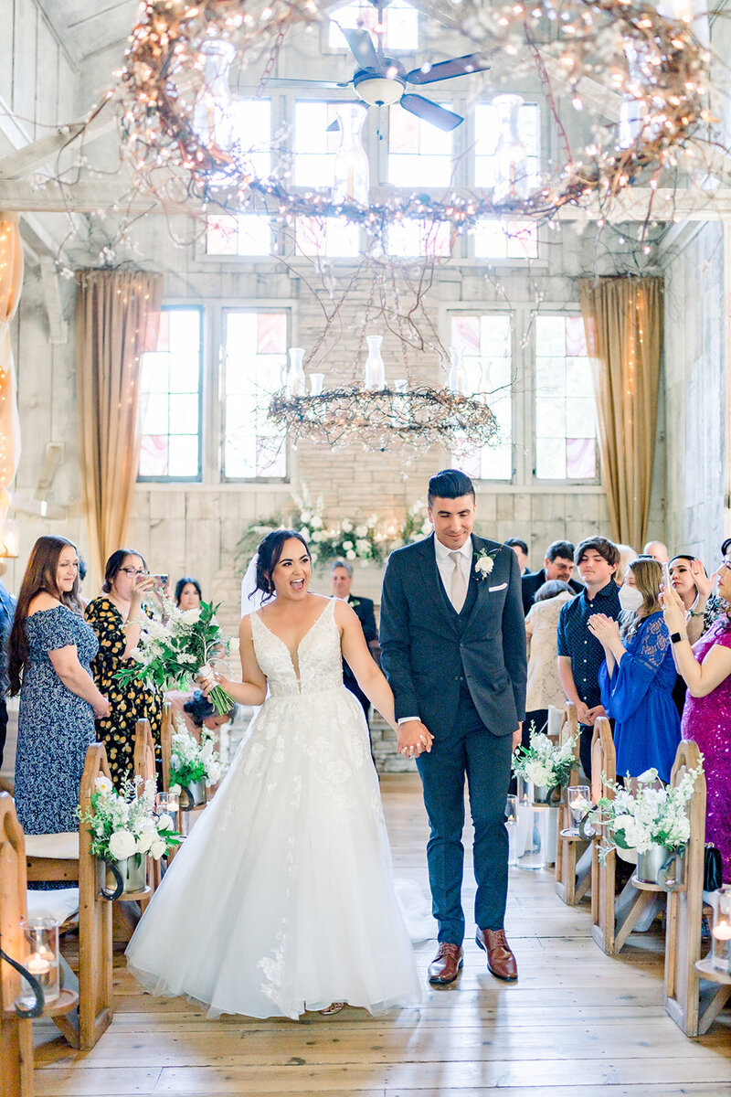 Tiffany Longeway Photography captures the elegance and joy of a newlywed couple walking down the aisle at The Estate Yountville in Napa Valley. The stunning indoor venue, adorned with intricate chandeliers and beautiful floral arrangements, provides a luxurious and romantic backdrop, ideal for couples seeking a sophisticated and enchanting wedding celebration.